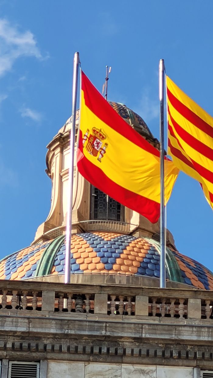 Spanish and Catalan flags atop a decorative dome in sunny Barcelona.